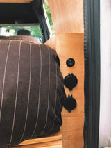 An RV rental's interior reveals a cozy pinstriped bed and a practical wood panel with a power switch & 12V outlets.