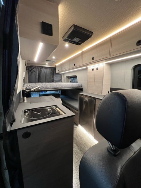 Bright and modern rv rental interior. Features strip lighting, integrated kitchen, controls, and storage.