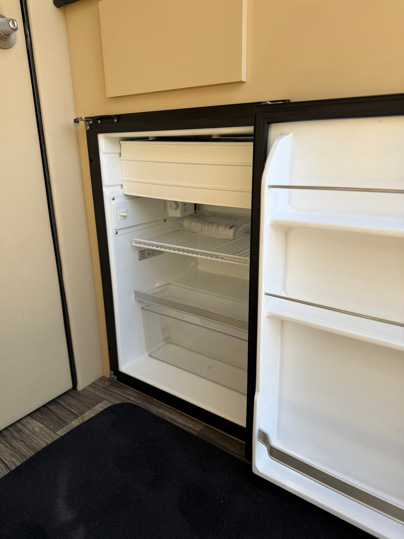 Clean, open mini-fridge in an rv rental, showing freezer, wire shelf, pull-out bin, and door storage. — photo 4