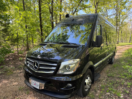 Black Mercedes Sprinter Airstream camper van parked in a sunlit forest, ideal for your next RV rental.