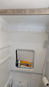 Compact RV rental wet bath with toilet, shower, and toiletries shelf.
