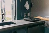 RV rental interior: compact kitchen with sink, induction cooktop, fridge, and control panel for comfortable mobile living.