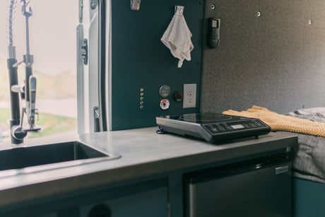 RV rental interior: compact kitchen with sink, induction cooktop, fridge, and control panel for comfortable mobile living.
