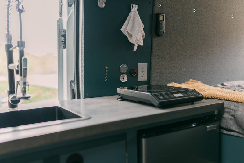 RV rental interior: compact kitchen with sink, induction cooktop, fridge, and control panel for comfortable mobile living. — photo 16