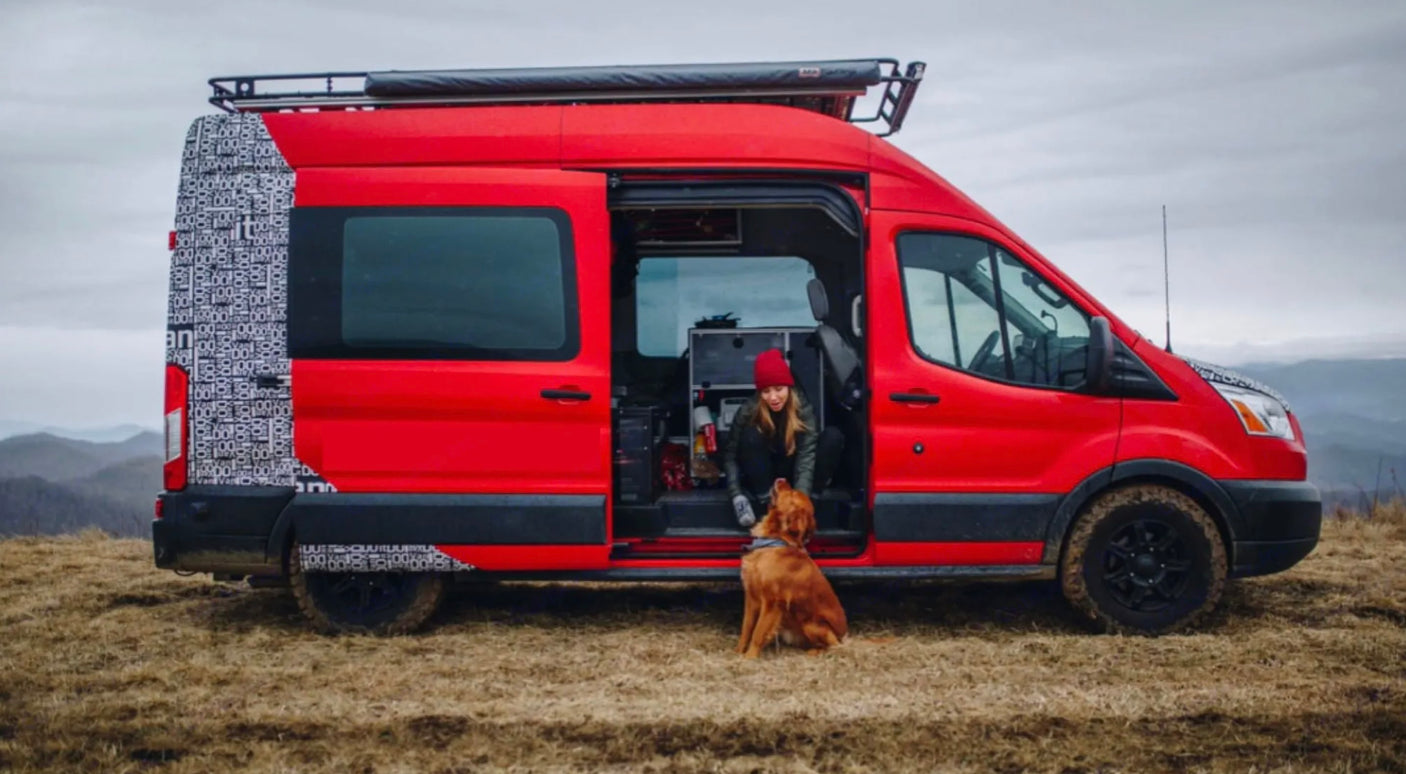 A woman and her dog relaxing in a customized red camper van, an ideal RV rental for outdoor adventures in the mountains.
