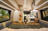 Inside an RV rental: a comfortable bed, functional kitchen, and scenic outdoor views through large windows.