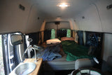 Cozy RV rental interior: bed, sink, and fans for comfortable camper van living or camping trips.