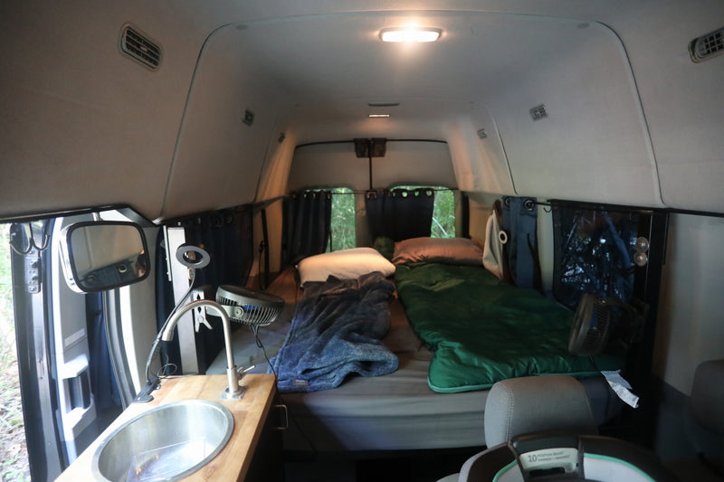  parked on a sunny dirt path in the woods.|Black Wandervans campervan RV rental parked in woods with open side door — photo 11