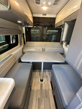 RV rental interior featuring a grey dinette with removable table, overhead cabinets, and wood-look flooring.