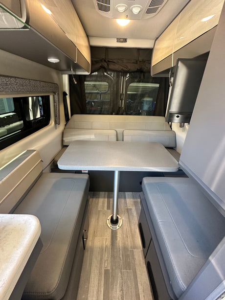RV rental interior featuring a grey dinette with removable table, overhead cabinets, and wood-look flooring.
