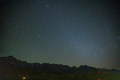 The dark night sky, filled with countless stars, stretches above silhouetted mountain ranges. Experience pristine nature on your RV rental adventure.