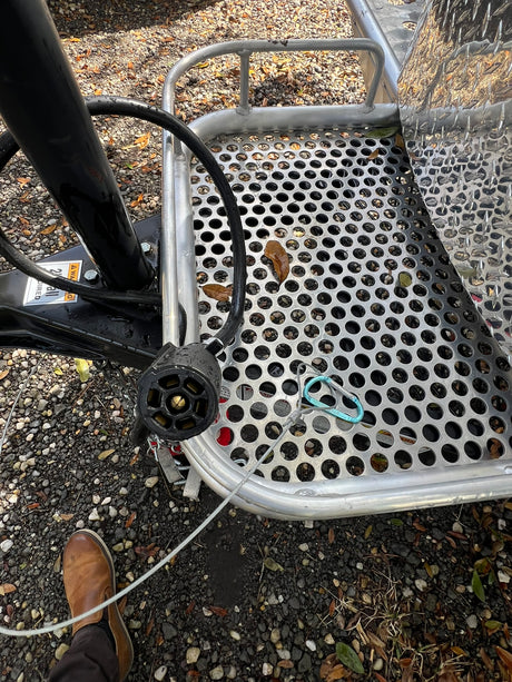 RV rental equipment: Hitch connection, 7-pin electrical connector, and perforated cargo carrier on a gravel surface.