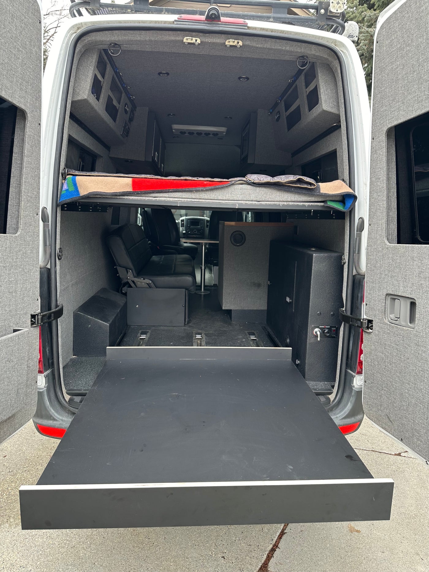 Rear view of an rv rental camper van conversion: elevated bed, seating, storage, and a large pull-out tray. — photo 4