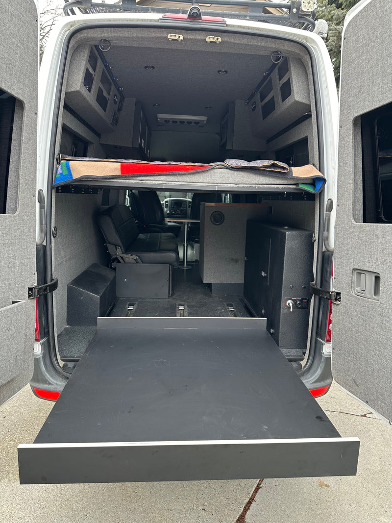 Rear view of an rv rental camper van conversion: elevated bed, seating, storage, and a large pull-out tray. — photo 4