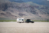 Explore off-grid with an rv rental: SUV towing a travel trailer across a dry lakebed, surrounded by arid mountains.