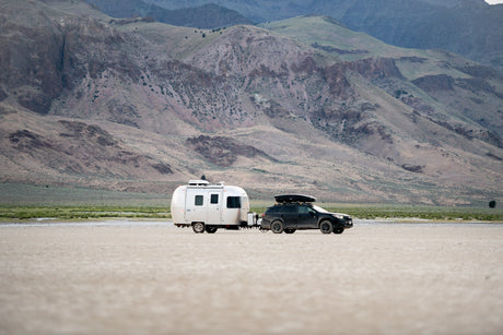 Explore off-grid with an rv rental: SUV towing a travel trailer across a dry lakebed, surrounded by arid mountains.