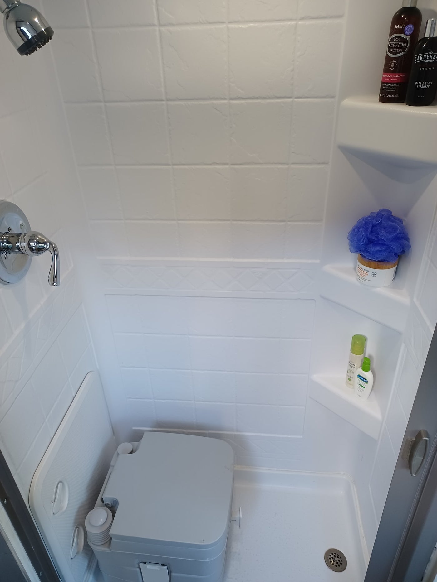 Inside an RV rental shower, showing a toilet, shower head, and toiletries: shampoo, body butter, Cetaphil lotion, and a loofah. — photo 2