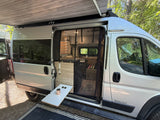 A silver Winnebago rv rental shows its open side with an extended awning, interior view, and pop-out table.