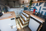 RV rental interior showing a bed, kitchen with sink & induction cooktop, plus many open storage drawers. Organized van life.