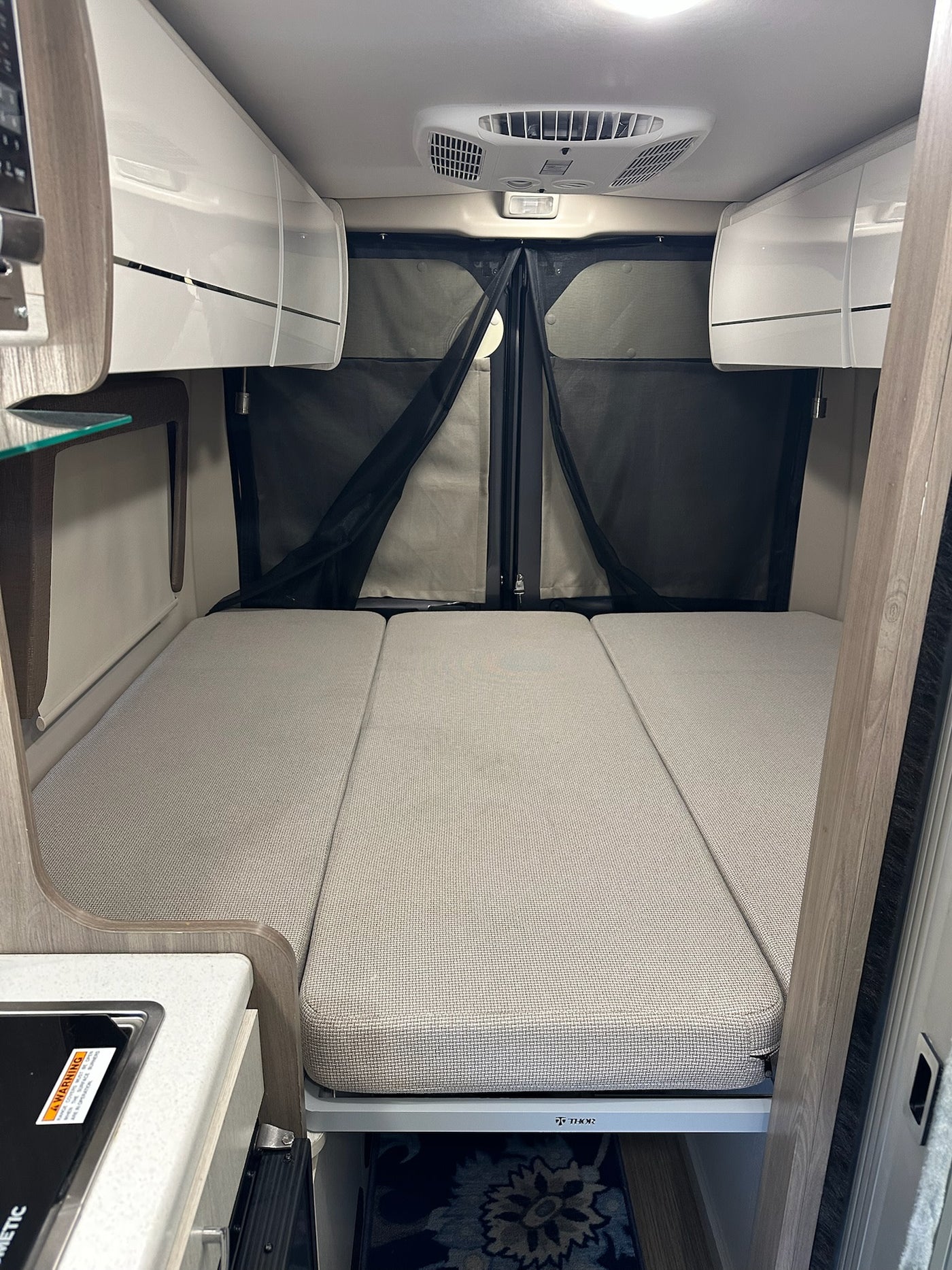  parked at a wooded campsite among tall trees.|Compact RV rental interior featuring a modern kitchen with sink — photo 3