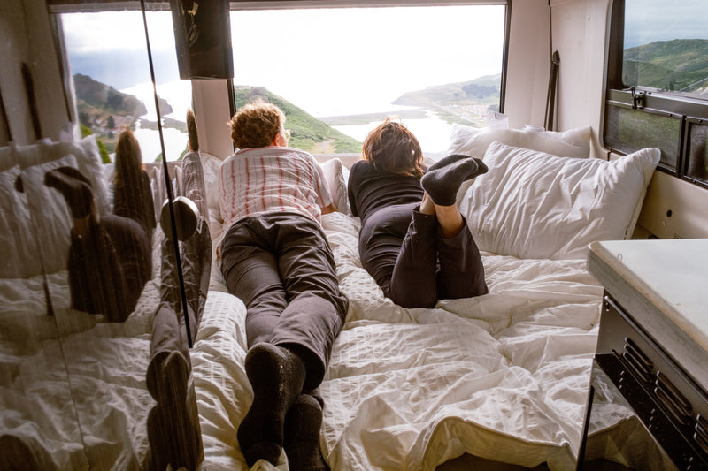 Enjoy the comfort of an RV rental. Two people relax on a bed admiring a panoramic coastal view. — photo 2