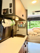 RV rental interior featuring a compact kitchenette with sink, faucet, paper towels, and storage, plus a cozy bed area.