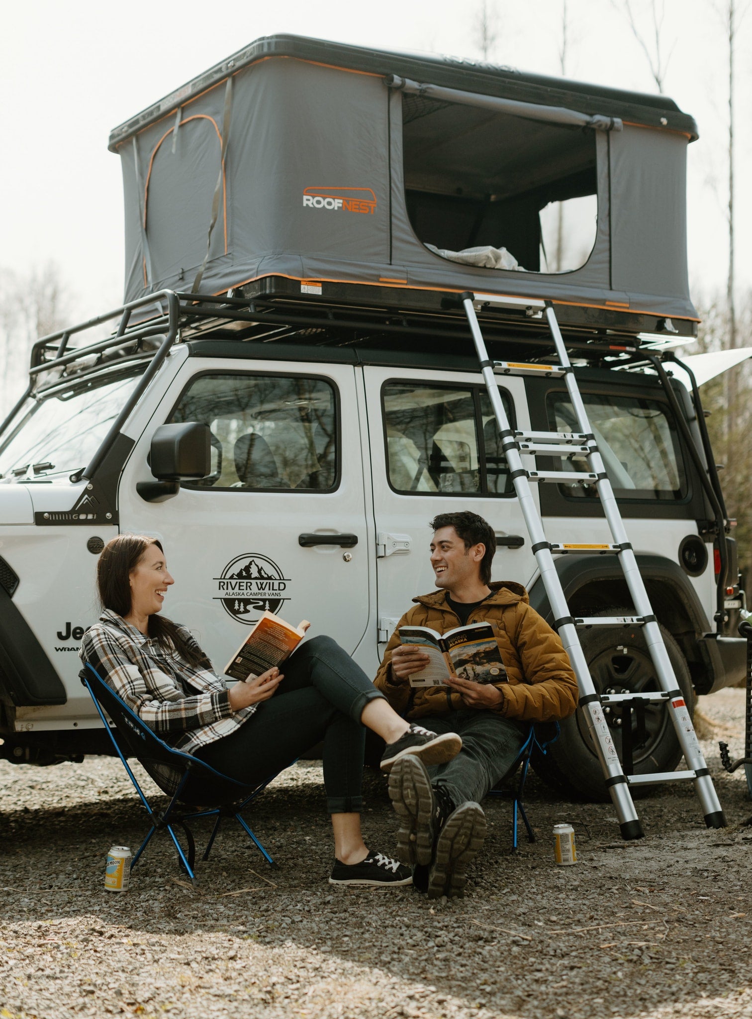 River Wild Alaska camper van (RV rental) with a Roofnest rooftop tent setup, two people relaxing & reading.