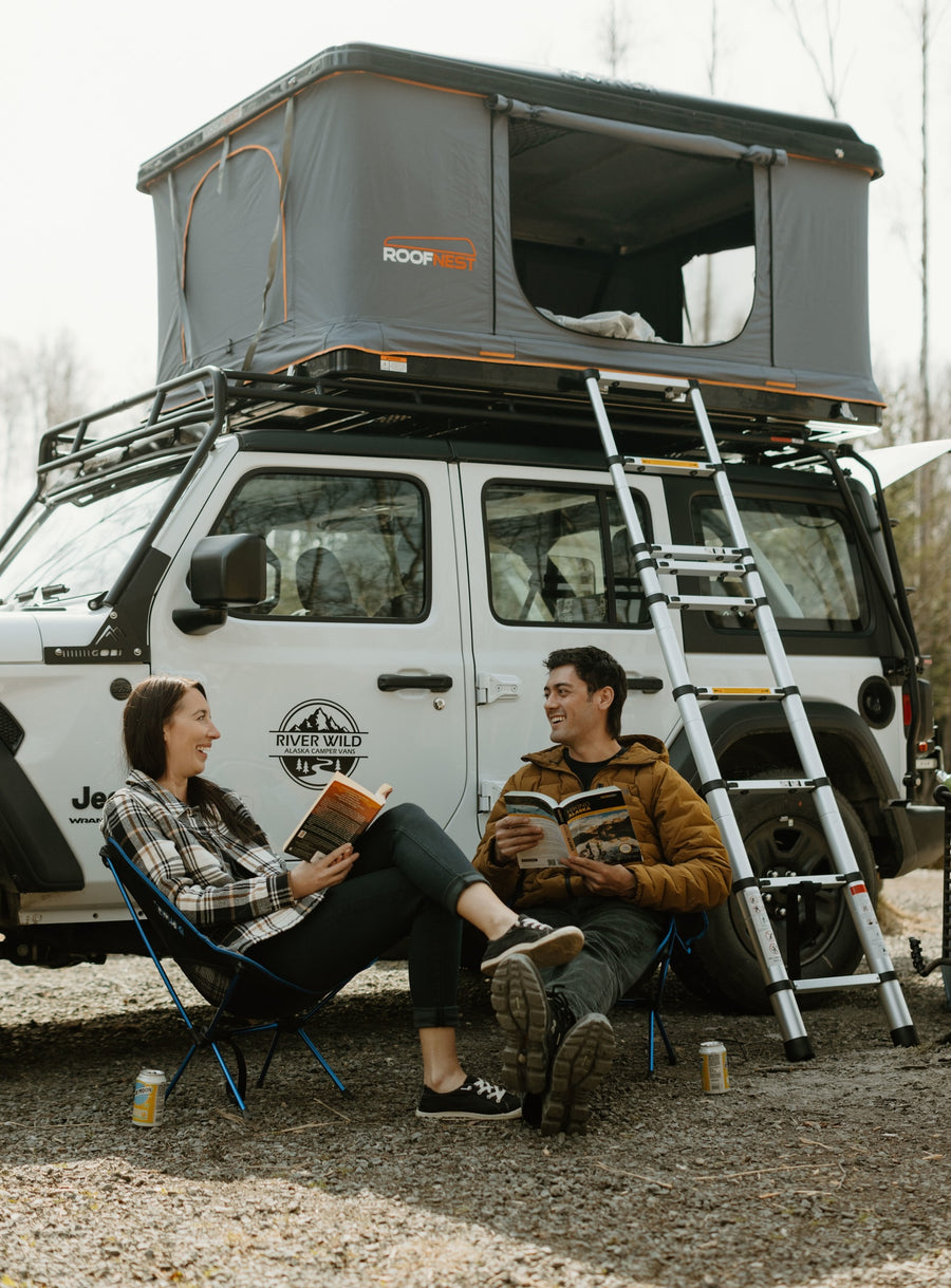 River Wild Alaska camper van (RV rental) with a Roofnest rooftop tent setup, two people relaxing & reading.