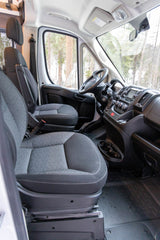 Spacious RV rental front cabin with grey seats, dashboard, and panoramic view of a wintry forest outside.