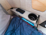 Cozy RV rental interior with sleeping bag, phone, cupholder, and a book. Perfect for comfortable travels.