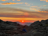 Vibrant sunrise over a rocky mountain campsite with tents. Picture this adventure after an RV rental trip!