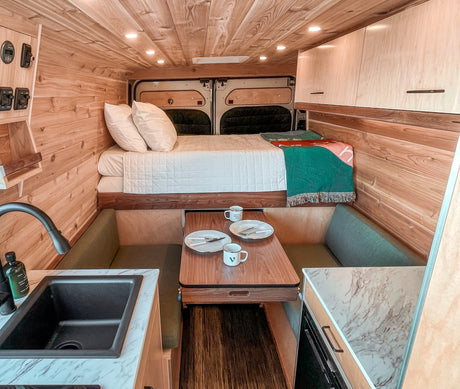 This RV rental's cozy wood interior showcases a raised bed, dining space with benches, and a functional kitchen sink.