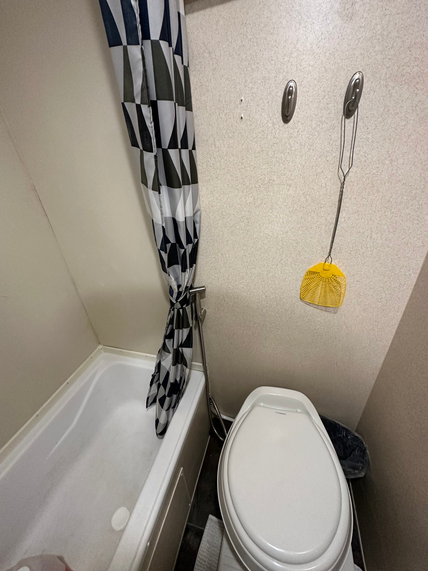 An RV rental's compact bathroom features a white tub, geometric shower curtain, Dometic toilet, and fly swatter.