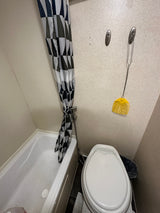 An RV rental's compact bathroom features a white tub, geometric shower curtain, Dometic toilet, and fly swatter.