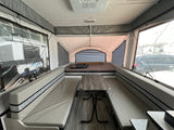 Interior of a light-toned pop-up camper RV rental, featuring a central dinette with benches and a rear bed.