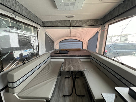 Interior of a light-toned pop-up camper RV rental, featuring a central dinette with benches and a rear bed.