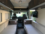 View inside a modern RV rental featuring a kitchen, two lounge sofas (convertible to beds), and the driver's area.