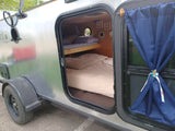 Inside a compact RV rental: a cozy sleeping area featuring bunk beds, nautical decor, and a porthole window.