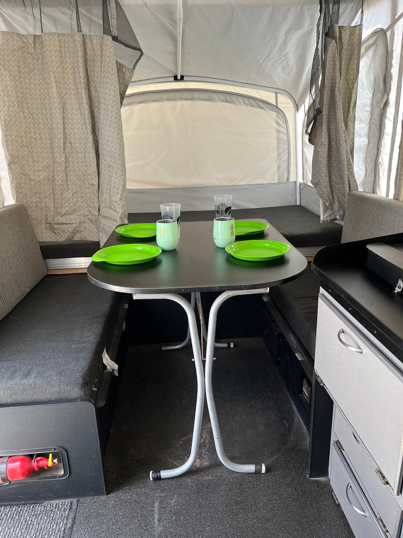RV rental interior: dining area with a table set for four, flanked by convertible beds and a small kitchen counter. — photo 12