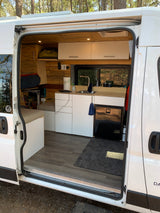 Spacious RV rental interior showcasing a custom-built kitchen, sleeping area, and storage with wood accents and white cabinets.