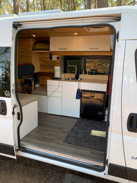 Spacious RV rental interior showcasing a custom-built kitchen, sleeping area, and storage with wood accents and white cabinets.
