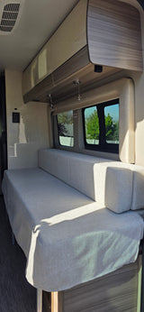 Modern RV rental interior featuring a versatile light gray bench seat/bed, ample overhead storage, and scenic windows.
