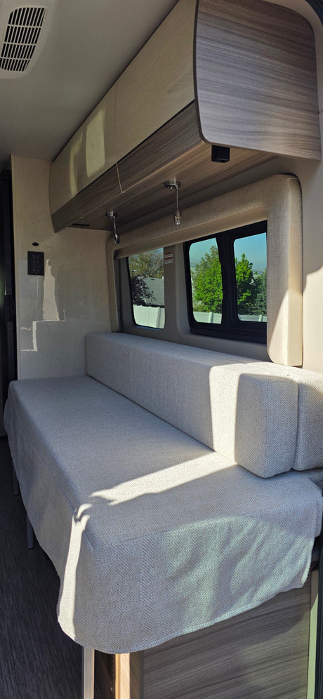 Modern RV rental interior featuring a versatile light gray bench seat/bed, ample overhead storage, and scenic windows.