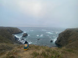 From a grassy cliff, a person gazes at the vast, misty ocean and rugged coastline. Ideal RV rental destination.