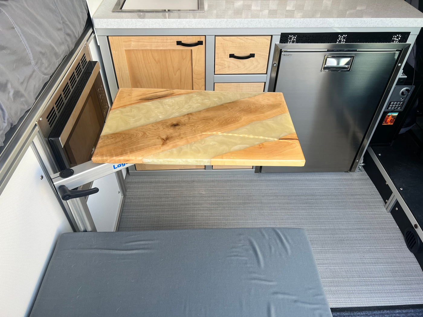 RV rental: Cozy camper van kitchen featuring a unique wood and resin table, fridge, microwave, and comfy bench. — photo 8