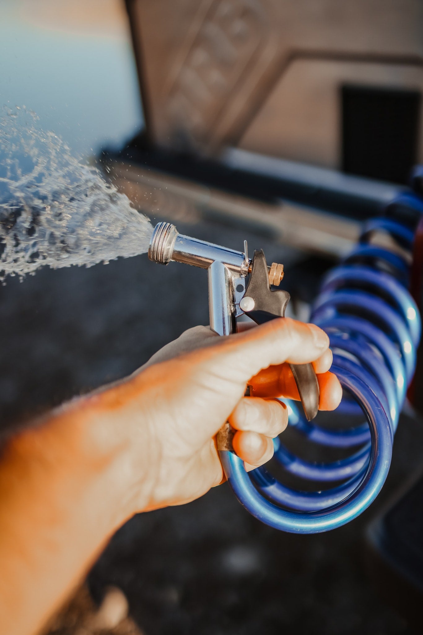 Hand spraying water from a nozzle connected to a coiled blue hose, likely cleaning an RV rental. — photo 6