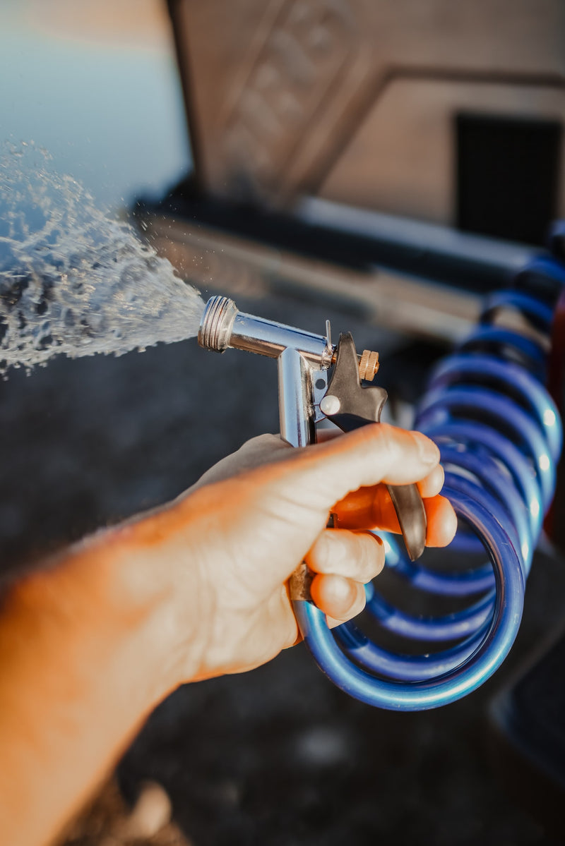 Hand spraying water from a nozzle connected to a coiled blue hose, likely cleaning an RV rental. — photo 6