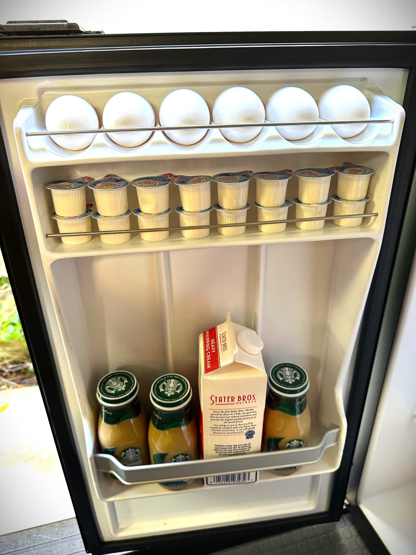 An organized RV rental mini-fridge. It holds 8 eggs, stacked coffee creamers, Starbucks bottled coffee, & whipping cream.