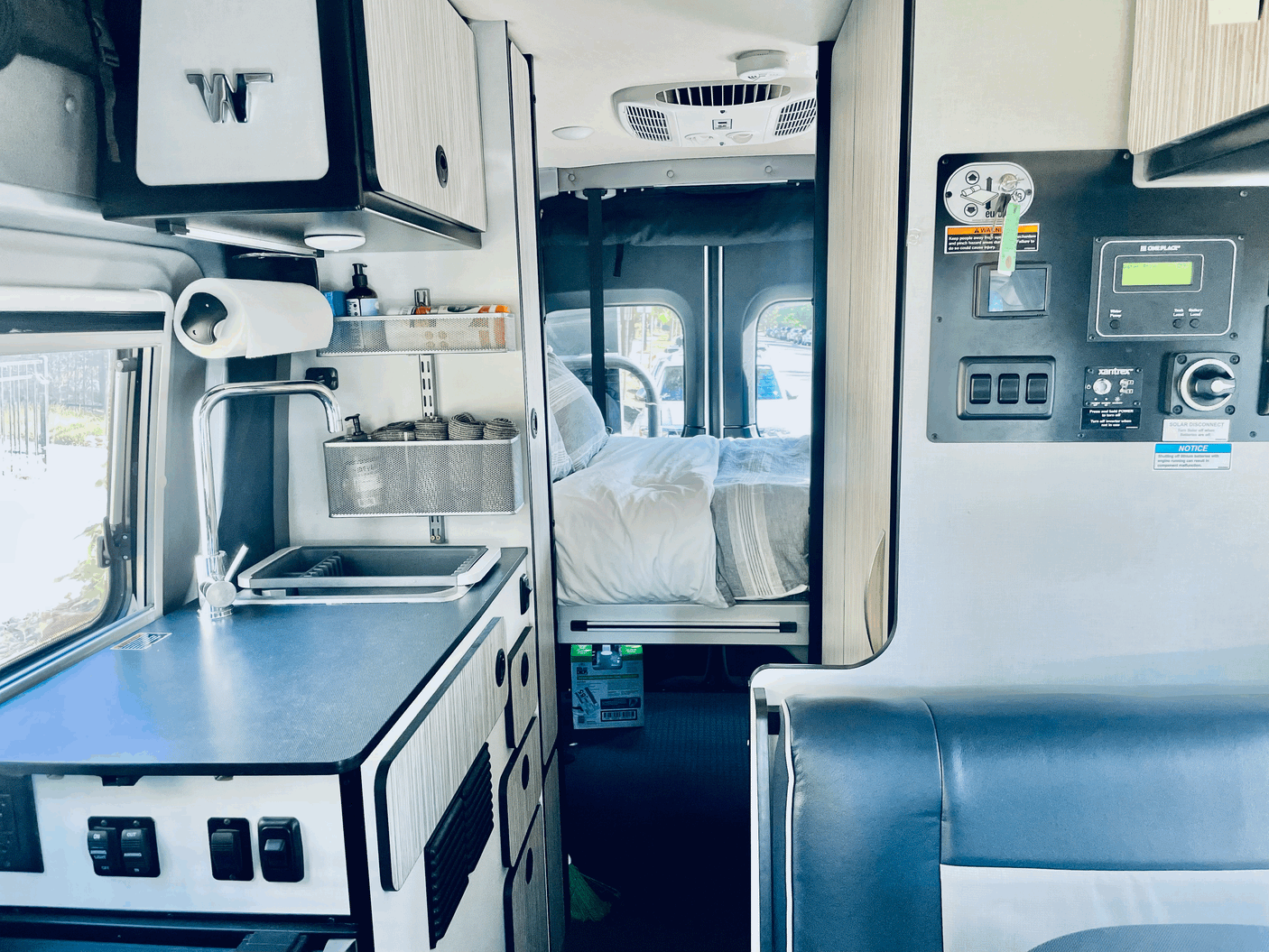 Interior view of an RV rental, featuring a compact kitchen, comfortable bed area, and control panel on the right.