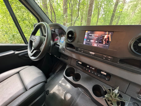 Experience comfort in this RV rental! Modern interior with dashboard, steering wheel, music playing, and a succulent plant by the cups.